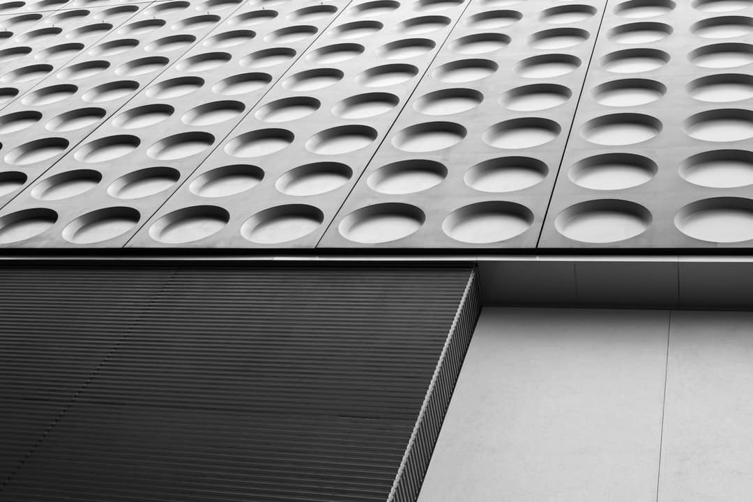 A facade of repeating circular openings over a dark base, in black and white