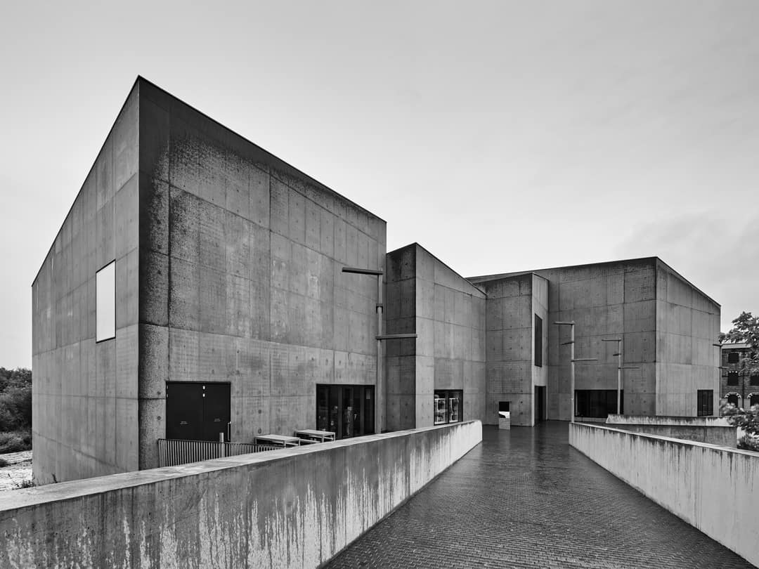 The angular concrete volumes of a gallery beside still water, in black and white