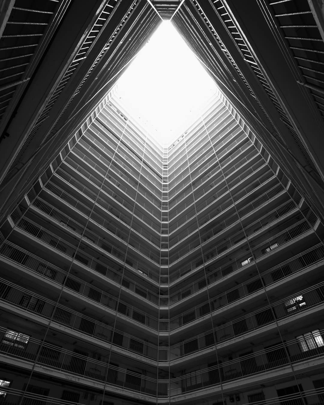 Looking up through the open core of a concrete housing block to the sky, in black and white