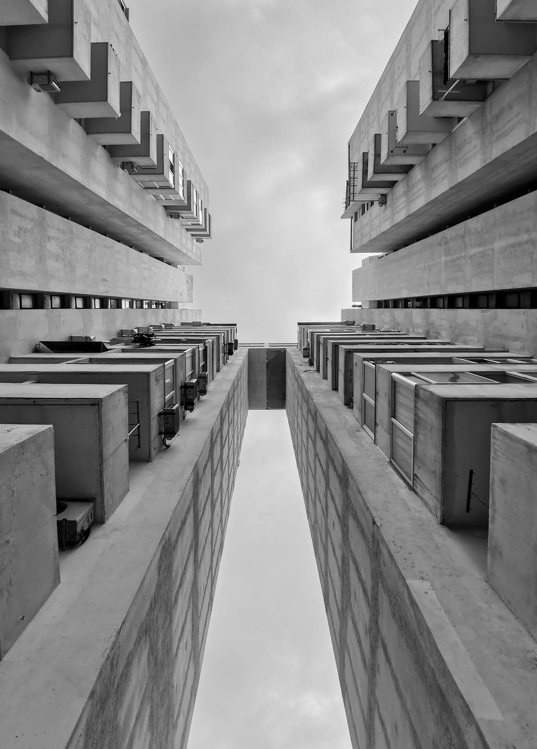Looking straight up a modernist concrete tower, in black and white
