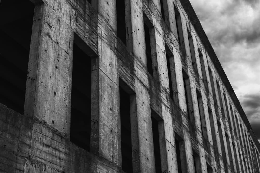 The bare concrete grid of an unfinished building under a stormy sky, in black and white